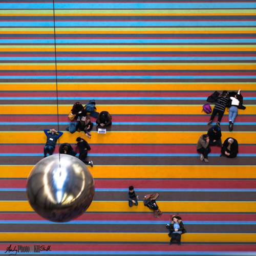 Silver ball swinging at people sat on a carpet at the Tate Modern