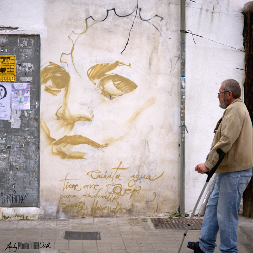 Man with stick looking af graffito of girl's face