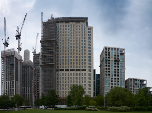 Lone man sitting in park in front of city buildings and cranes