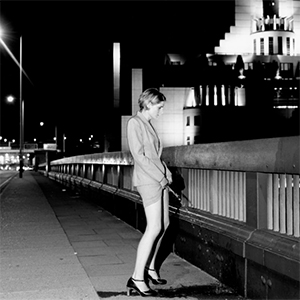 Author herself, dressed in smart city clothes, urinating like a man on bridge with the MI6 building in the background