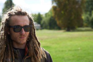 White guy with shades and deadlocks looking away from camera