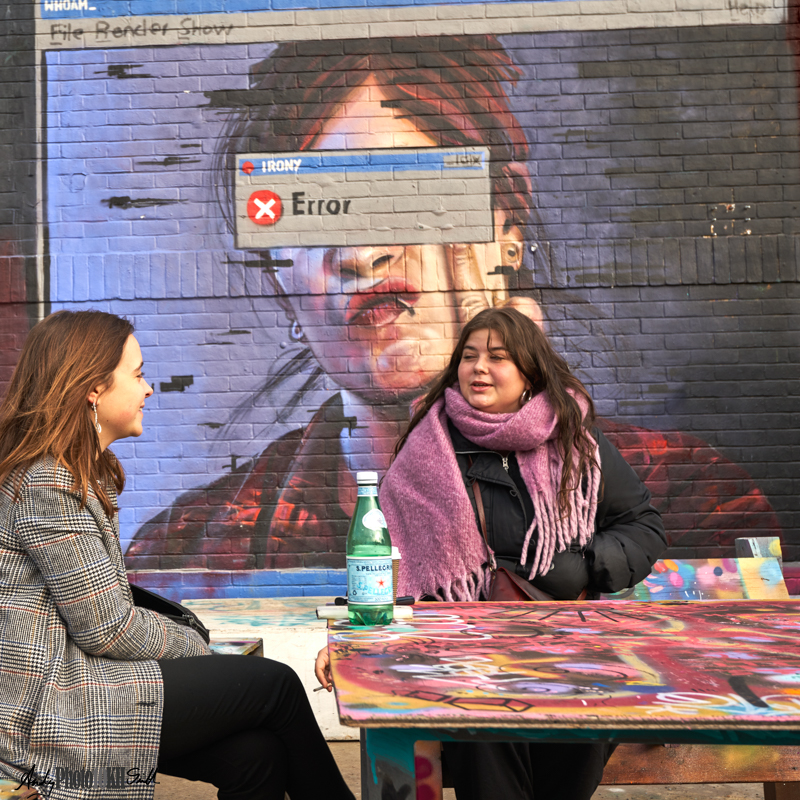 Two women drinking posh bottled water in front of an irony graffito.  Learning photography autumn