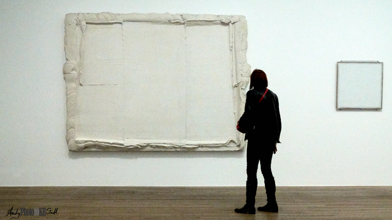 Woman looking at an all white painting in the room "painting with white"