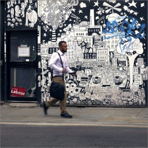 Man walking past a sign for labour towards blue graffiti tag
