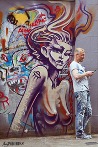 Man standing in front of fantasy graffiti of topless woman with devil caricature behind her 