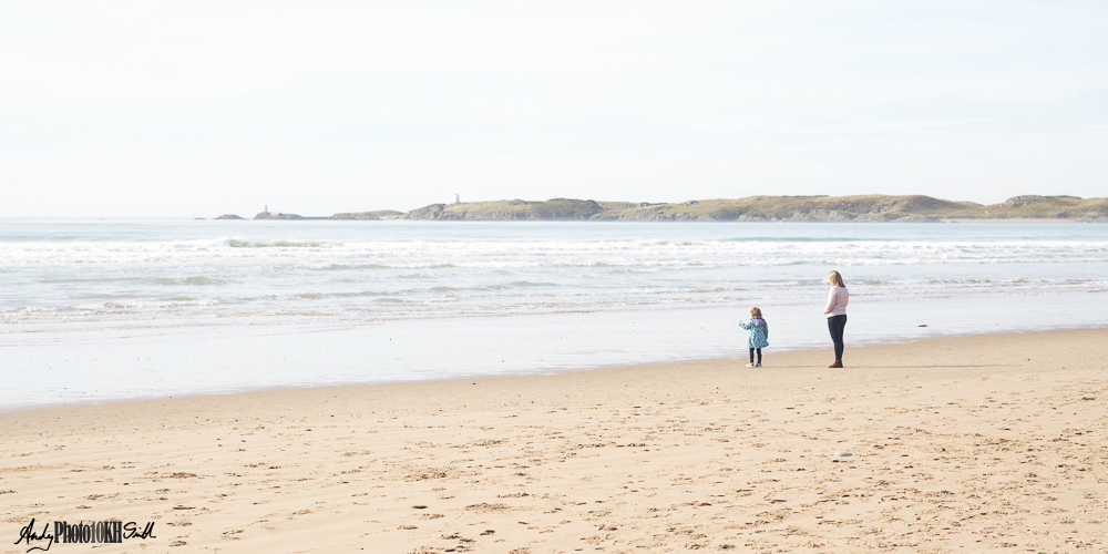 Mother and daughter standing at the shoreline looking out to sea