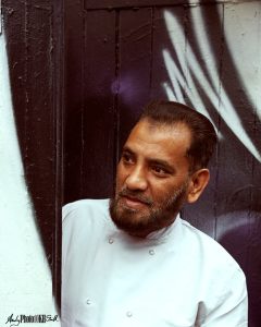Chef appearing from behind a graffiti covered door in Brick Lane